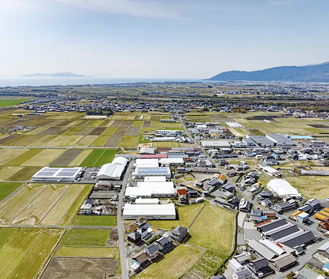 上空から見た湖岸の町と田園地帯。琵琶湖沿いに広がる街並みと田畑が一望できる、地域の豊かな自然と暮らしを示す風景。