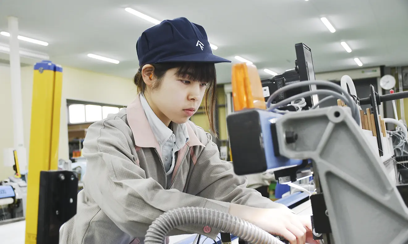 作業服と帽子を着用した女性社員が、機械の操作に集中している。